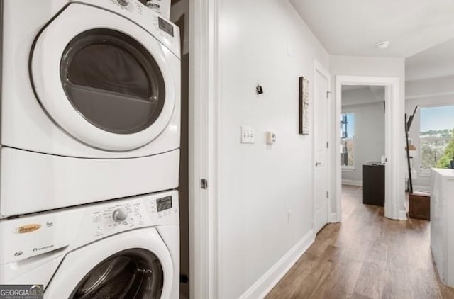 washroom with laundry area, wood finished floors, baseboards, and stacked washing maching and dryer