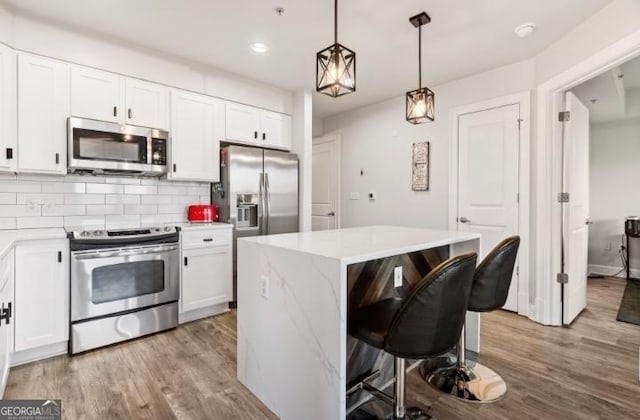 kitchen featuring backsplash, a kitchen bar, light wood-style flooring, white cabinets, and stainless steel appliances