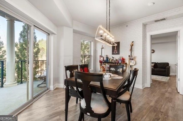 dining space featuring wood finished floors, visible vents, brick wall, and baseboards