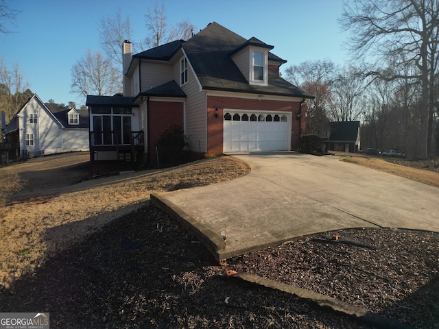 view of home's exterior with a sunroom, brick siding, driveway, and a chimney