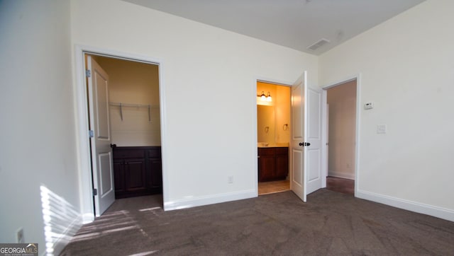 unfurnished bedroom with dark colored carpet, visible vents, baseboards, and ensuite bath