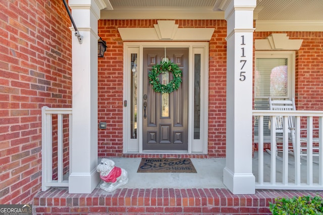 view of exterior entry with brick siding and covered porch