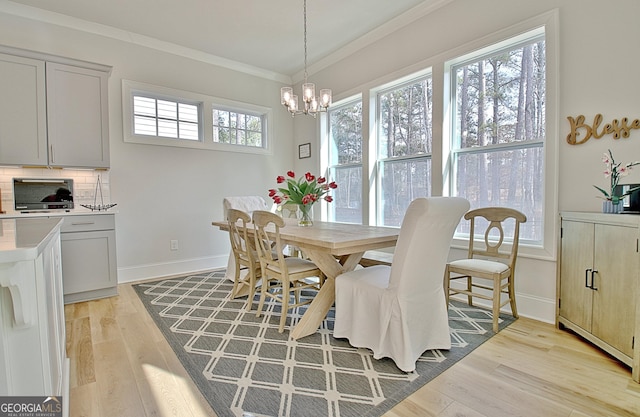 dining space with light wood-style flooring, a notable chandelier, baseboards, and ornamental molding