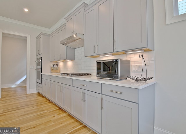 kitchen with under cabinet range hood, stainless steel appliances, light wood-style floors, and gray cabinets