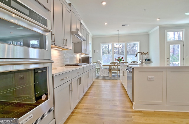 kitchen featuring tasteful backsplash, visible vents, ornamental molding, light wood-style flooring, and appliances with stainless steel finishes