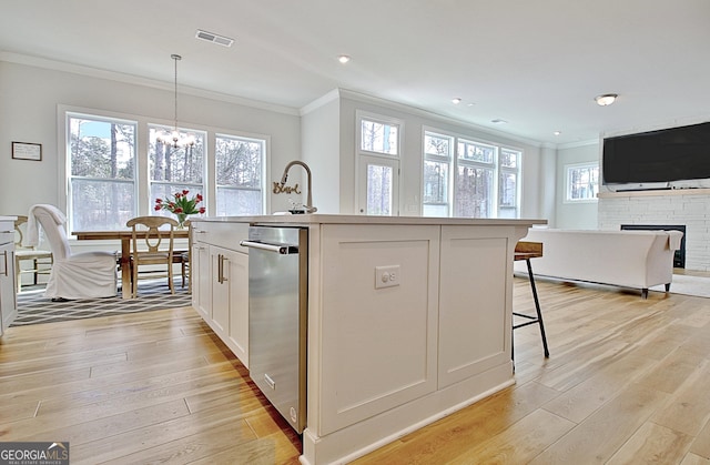 kitchen with visible vents, open floor plan, light wood-type flooring, ornamental molding, and a kitchen island with sink