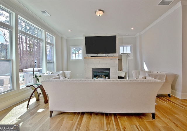 living area featuring light wood-style floors, crown molding, a fireplace, and visible vents