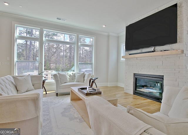 living area featuring baseboards, visible vents, a fireplace, ornamental molding, and light wood-type flooring