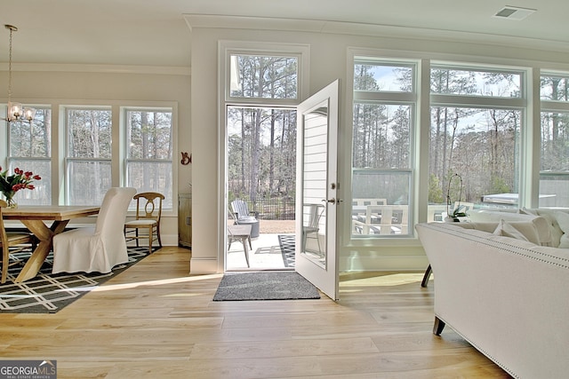 doorway with visible vents, a chandelier, ornamental molding, and light wood finished floors