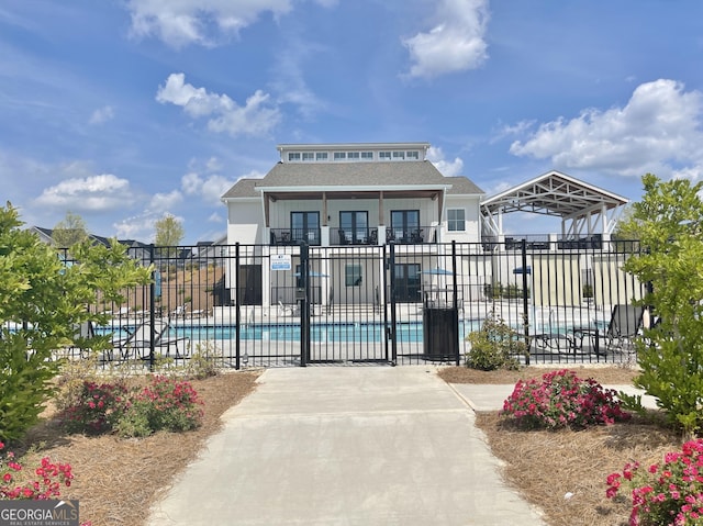 view of front facade featuring a community pool, roof with shingles, and fence