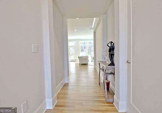 hallway featuring baseboards, visible vents, and light wood finished floors