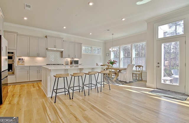 kitchen with decorative backsplash, light countertops, light wood-style flooring, and visible vents