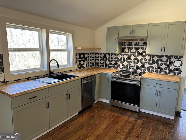 kitchen with a sink, under cabinet range hood, stainless steel appliances, butcher block counters, and vaulted ceiling