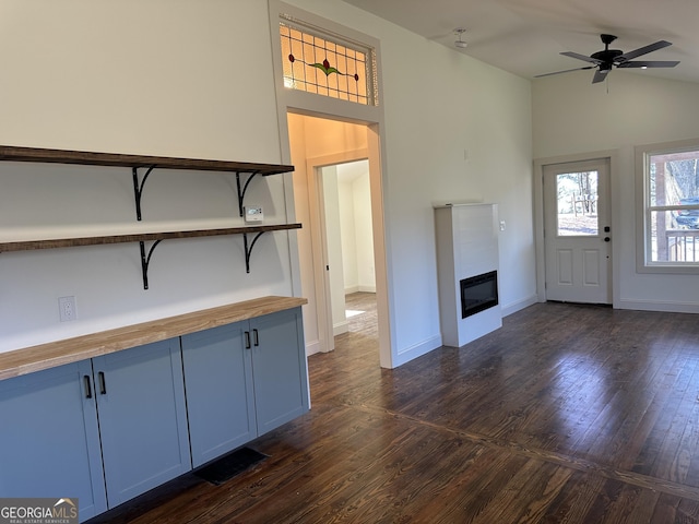 unfurnished living room with a ceiling fan, baseboards, dark wood finished floors, vaulted ceiling, and a glass covered fireplace