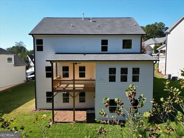 rear view of house with a shingled roof, a yard, and a ceiling fan