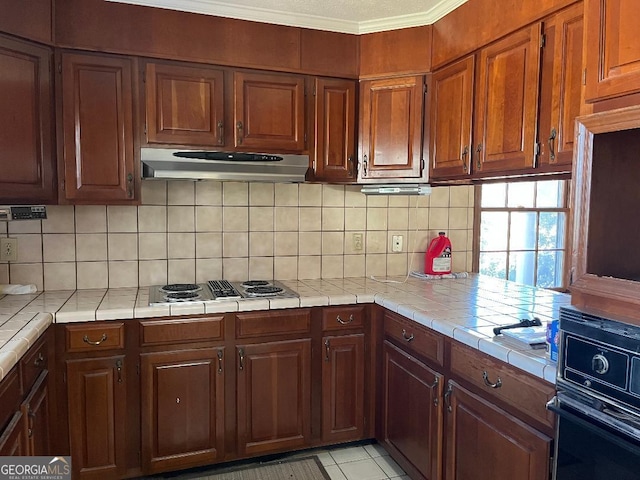 kitchen with tile countertops, oven, stovetop with downdraft, under cabinet range hood, and tasteful backsplash