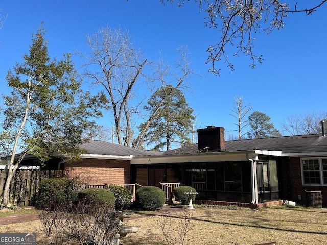 back of property featuring cooling unit, a yard, a sunroom, a chimney, and brick siding