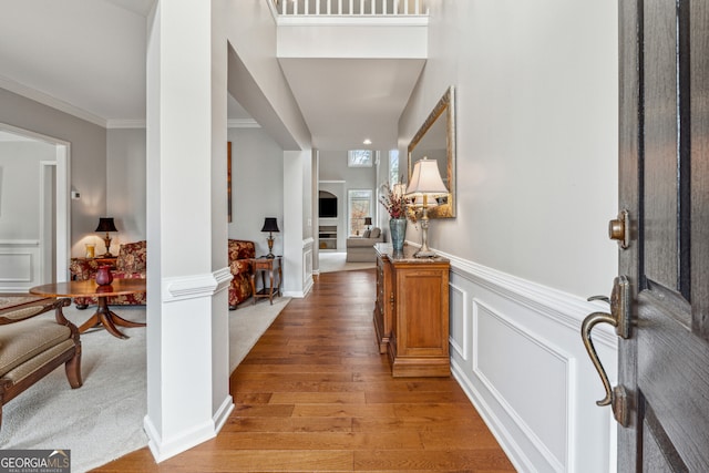 entrance foyer with a decorative wall, crown molding, light wood-style floors, and a wainscoted wall