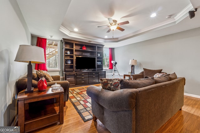 living room with crown molding, a ceiling fan, light wood-style floors, and a tray ceiling