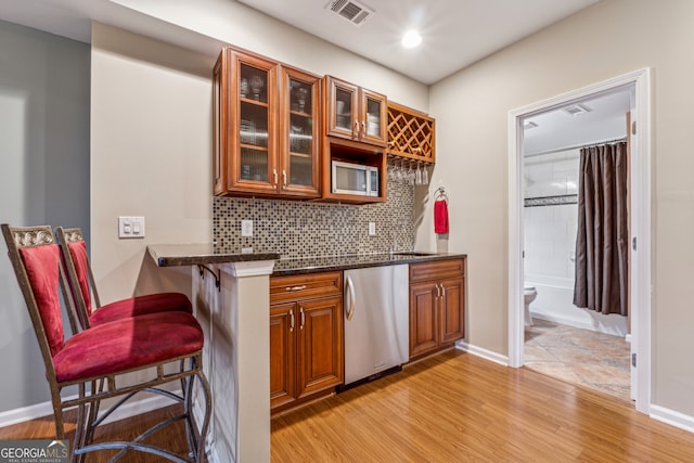 bar with visible vents, baseboards, light wood-style floors, dishwasher, and tasteful backsplash