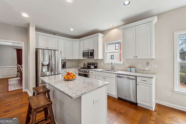 kitchen with a sink, a breakfast bar, appliances with stainless steel finishes, white cabinets, and dark wood-style flooring