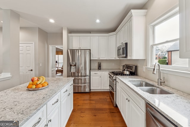 kitchen with a sink, appliances with stainless steel finishes, wood finished floors, and white cabinetry