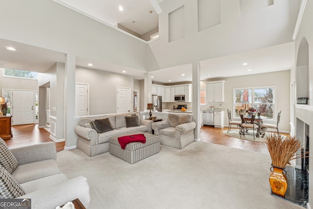 living room with recessed lighting, light wood-style floors, a high ceiling, baseboards, and light colored carpet