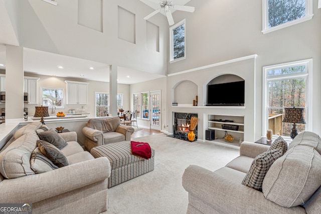 carpeted living room featuring a ceiling fan, built in features, a healthy amount of sunlight, and a high end fireplace