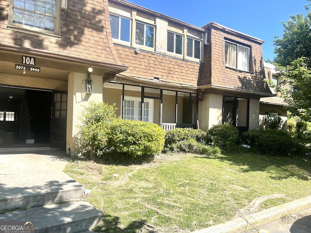 view of front of property featuring a shingled roof, a front yard, mansard roof, and stucco siding