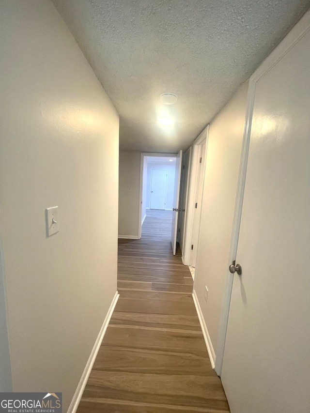corridor with baseboards, wood finished floors, and a textured ceiling