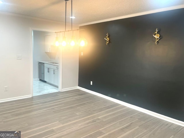 unfurnished dining area featuring crown molding, a textured ceiling, light wood finished floors, and baseboards