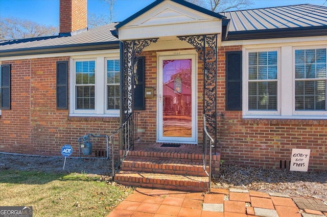 property entrance with metal roof, brick siding, a chimney, and a standing seam roof