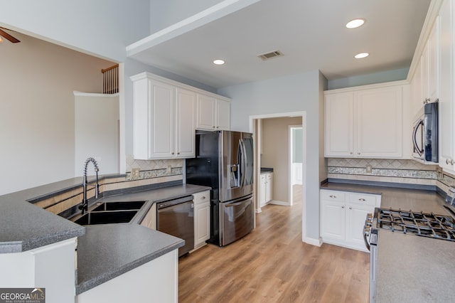 kitchen with dark countertops, visible vents, appliances with stainless steel finishes, white cabinets, and a sink