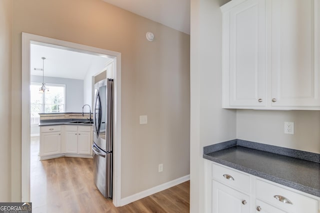 kitchen with dark countertops, freestanding refrigerator, light wood-style floors, white cabinets, and a sink