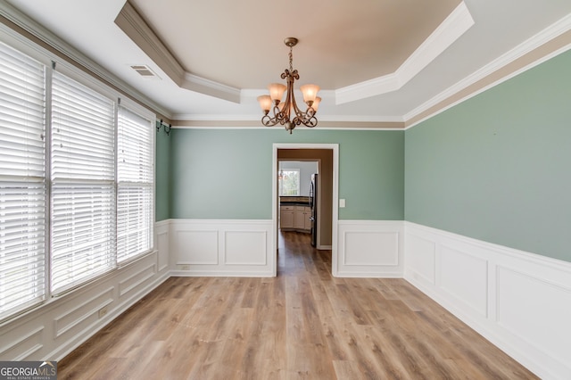 unfurnished room featuring visible vents, a wainscoted wall, light wood-style flooring, a notable chandelier, and a raised ceiling