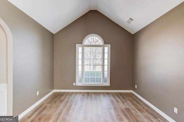 unfurnished room featuring light wood-type flooring, visible vents, arched walkways, baseboards, and vaulted ceiling