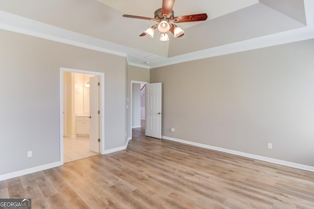 unfurnished bedroom with a tray ceiling, baseboards, crown molding, and light wood finished floors