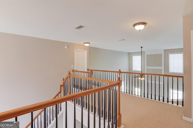 hall featuring carpet flooring, an upstairs landing, and visible vents