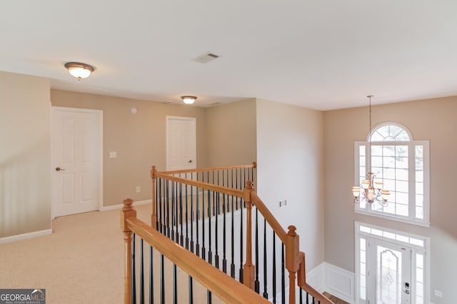 hall featuring visible vents, an upstairs landing, carpet floors, and an inviting chandelier