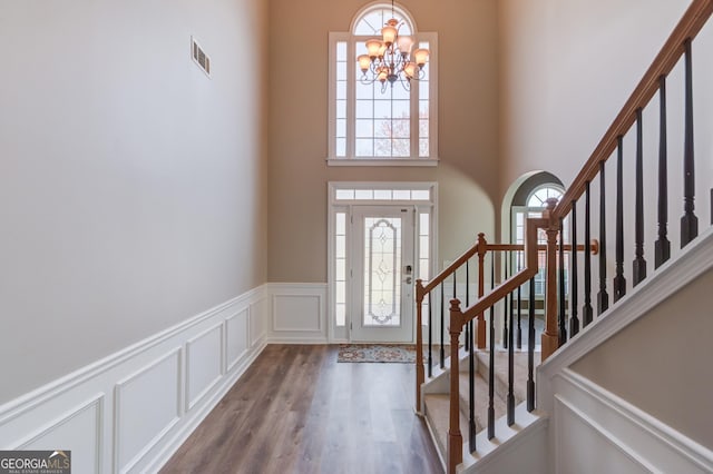 entryway with visible vents, wood finished floors, a decorative wall, a chandelier, and stairs