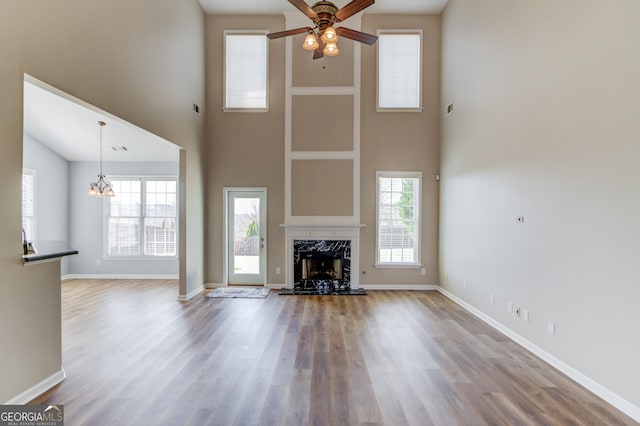 unfurnished living room featuring a high end fireplace, ceiling fan with notable chandelier, a healthy amount of sunlight, and wood finished floors