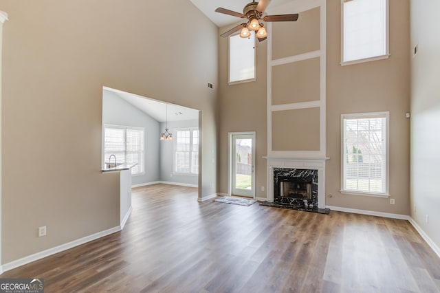 unfurnished living room featuring wood finished floors, ceiling fan with notable chandelier, baseboards, and a premium fireplace