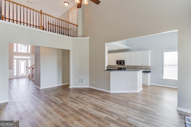 unfurnished living room with light wood-style floors, a towering ceiling, and ceiling fan