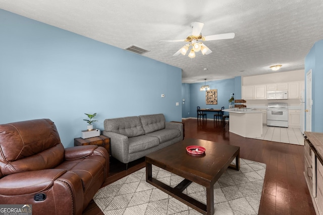 living area featuring light wood-type flooring, visible vents, a textured ceiling, and ceiling fan