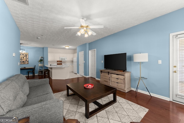 living room with a textured ceiling, light wood-style flooring, baseboards, and ceiling fan