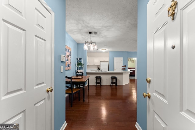 corridor with visible vents, dark wood-style flooring, a sink, a textured ceiling, and a notable chandelier