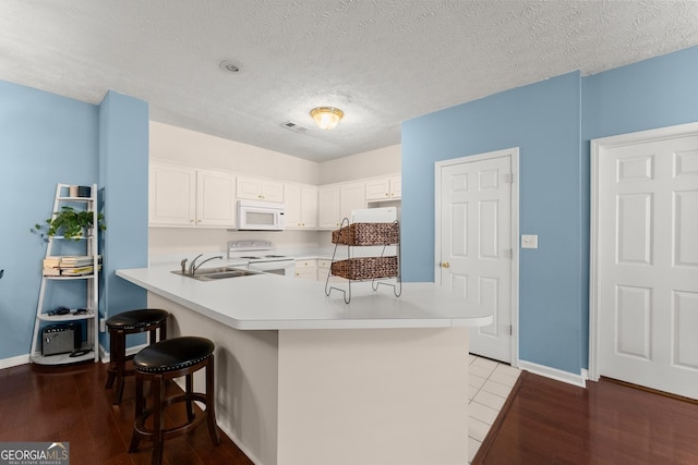 kitchen featuring white appliances, wood finished floors, a sink, light countertops, and a kitchen bar