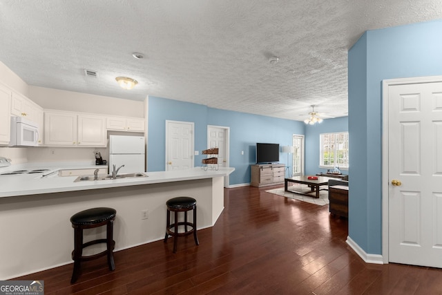 kitchen featuring visible vents, a breakfast bar area, a peninsula, white appliances, and dark wood-style flooring