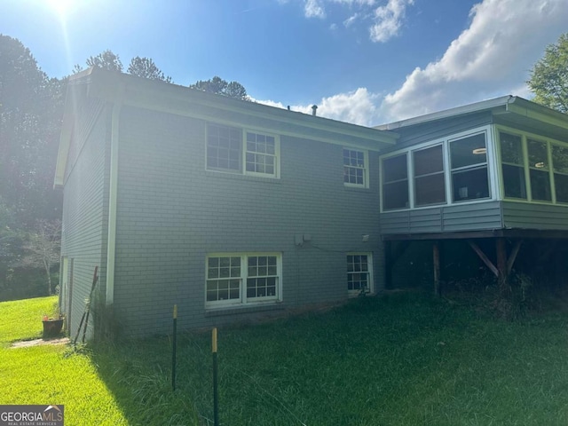 back of house featuring a yard, brick siding, and a sunroom