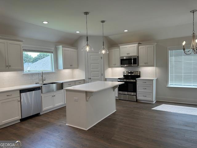 kitchen featuring dark wood finished floors, a sink, stainless steel appliances, white cabinetry, and a notable chandelier